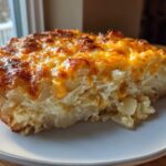 A close-up of a thick slice of creamy potato casserole with a golden, bubbly, cheesy crust.