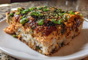 A close-up, featured shot of a square slice of amazing sushi bake on a white plate.