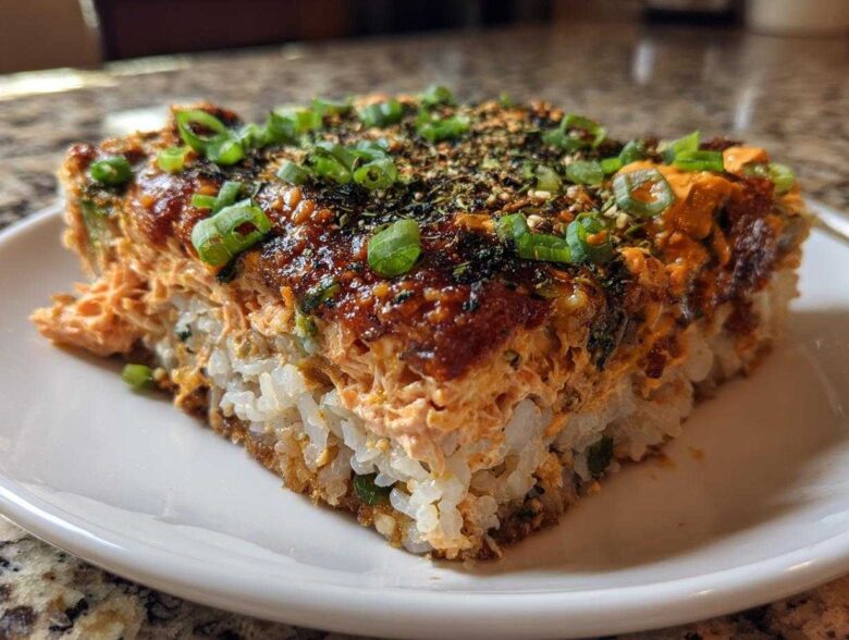 A close-up, featured shot of a square slice of amazing sushi bake on a white plate.