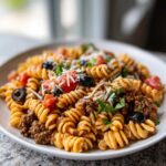 A close-up view of a serving of amazing taco pasta salad featuring rotini pasta, ground meat, diced tomatoes, black olives, and shredded cheese.