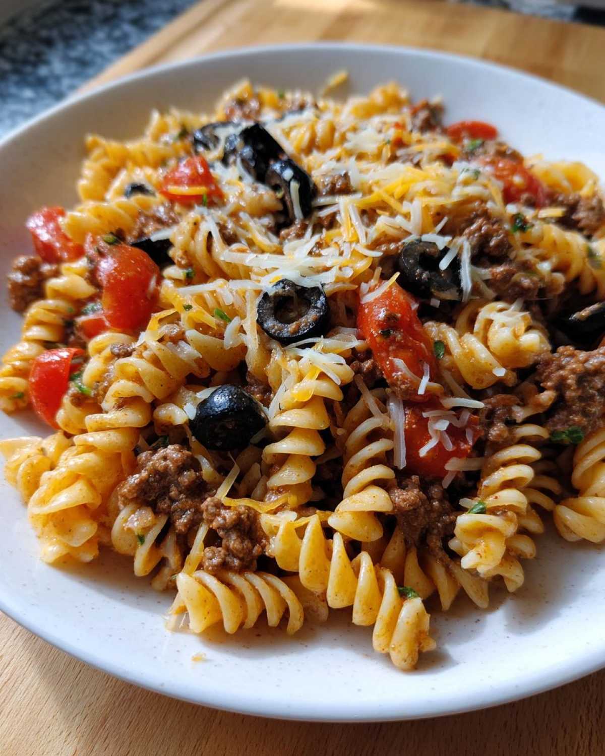 A close-up serving of amazing taco pasta salad featuring rotini pasta, seasoned ground beef, black olives, tomatoes, and shredded cheese.