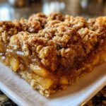 Close-up of a thick, gooey slice from an apple crisp recipe showing caramelized apples and a thick oat crumble topping.