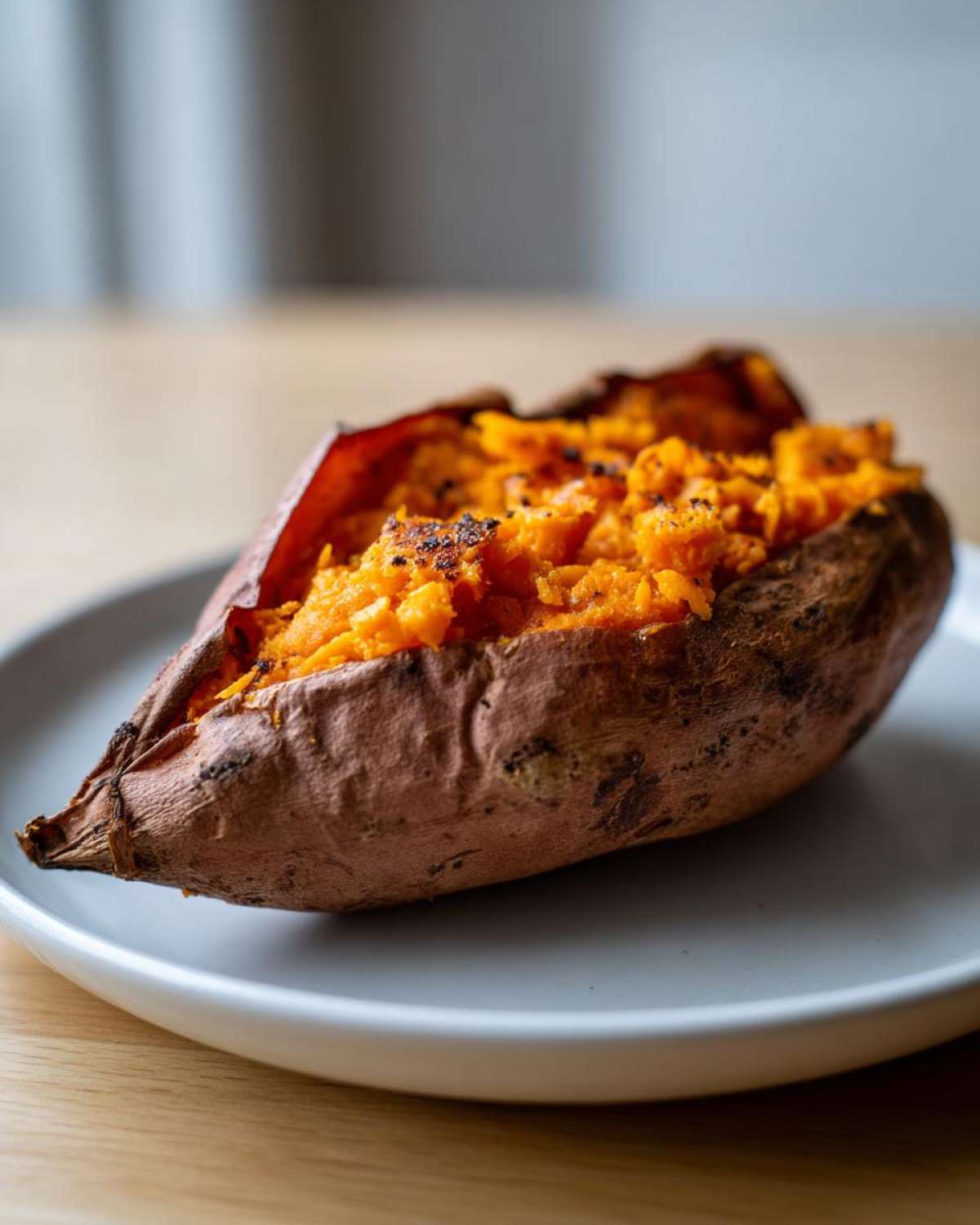A close-up of a single baked sweet potatoes, split open to show the bright orange, fluffy interior.