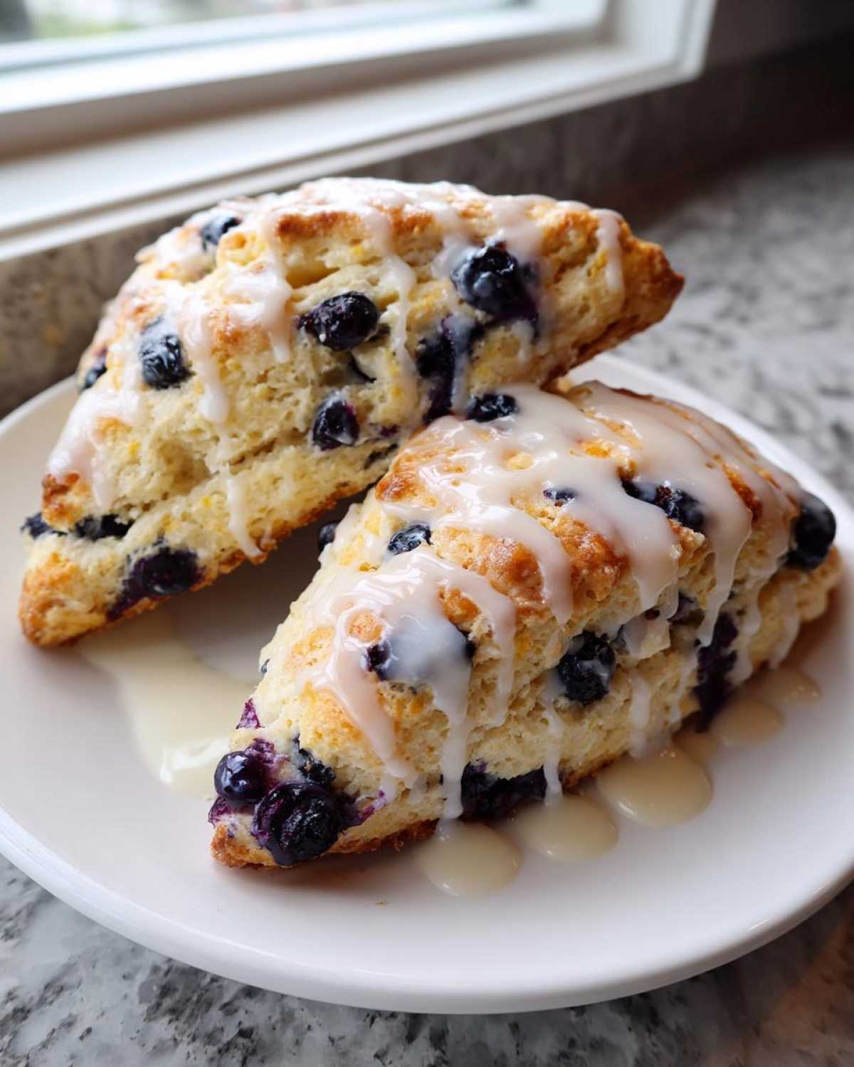 Two triangular blueberry scones topped with a thick vanilla glaze, sitting on a white plate.