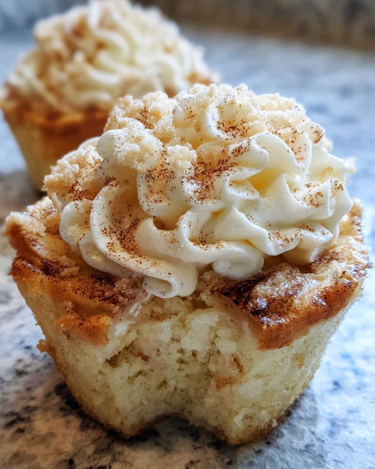 Close-up of a banana pudding cupcakes with a bite taken out, showing the crumb and vanilla frosting dusted with cinnamon.