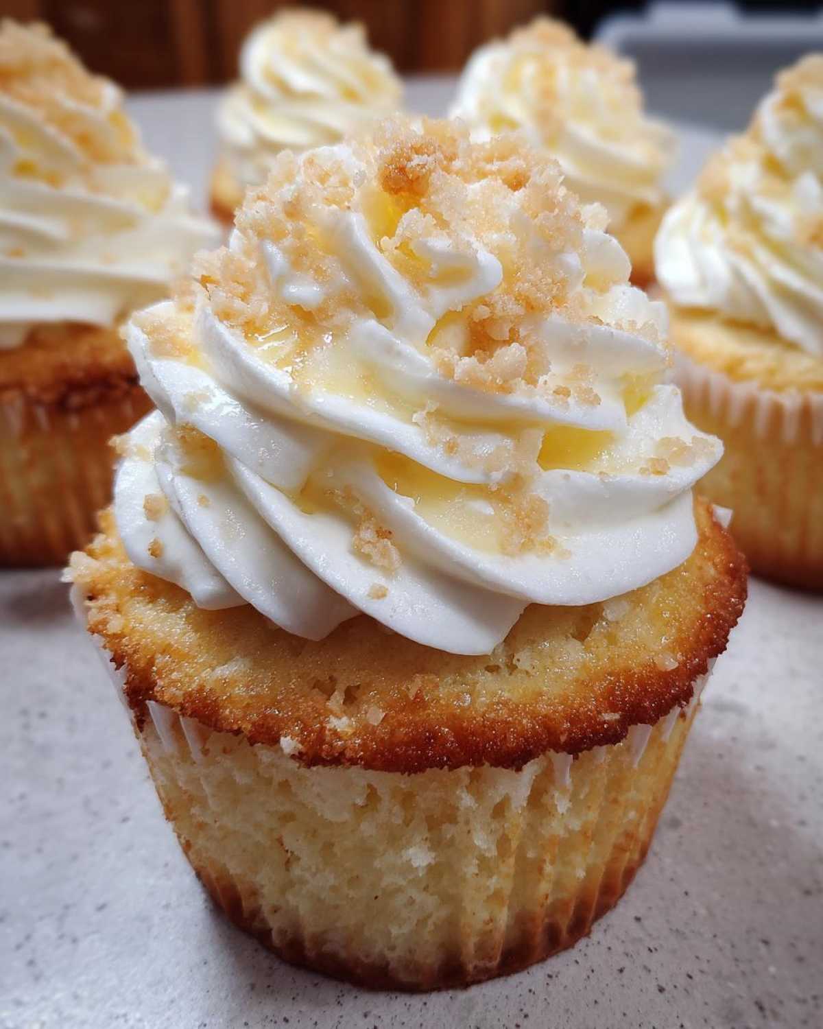 Close-up of a single banana pudding cupcakes topped with white frosting, crushed wafers, and a drizzle of glaze.