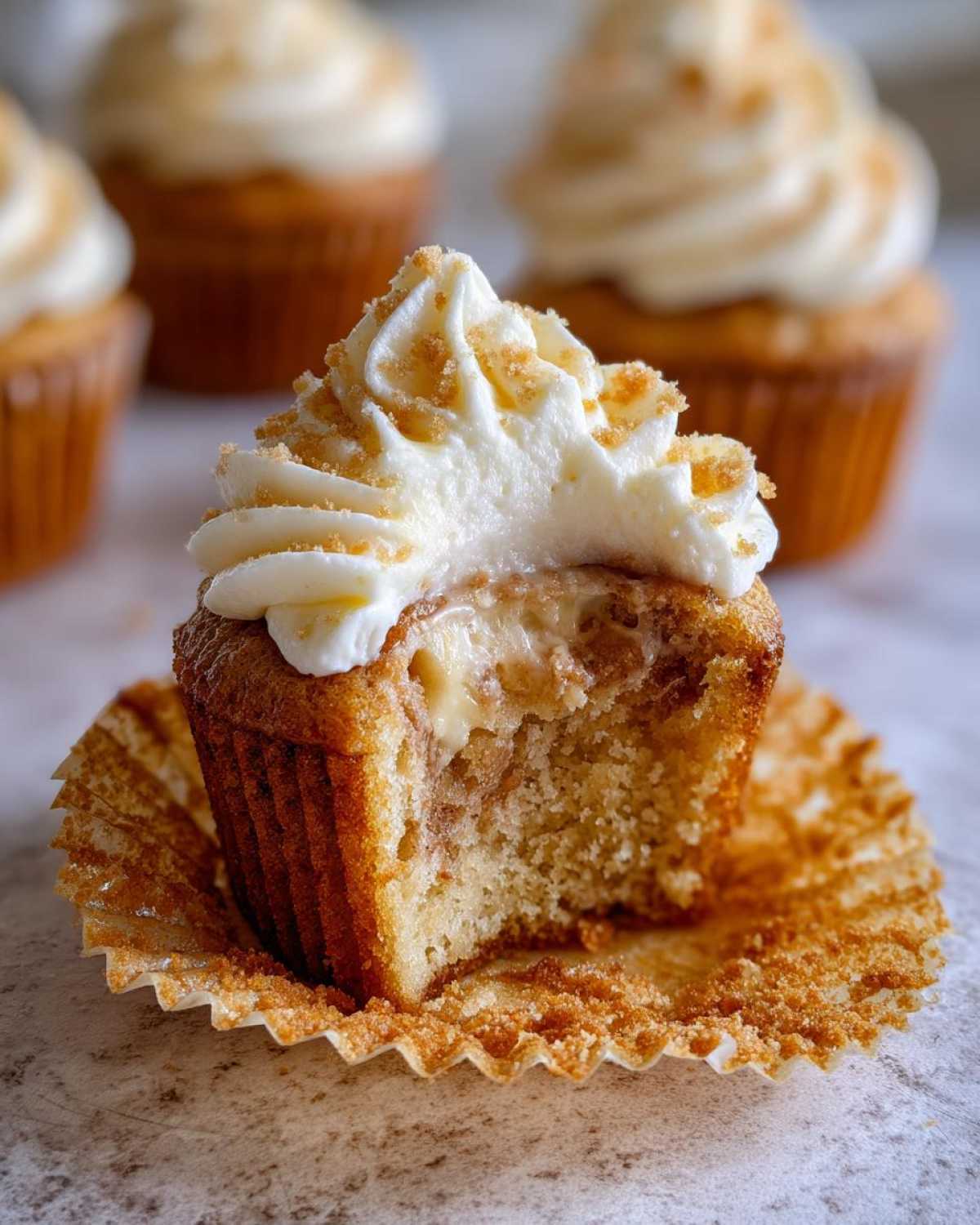 Close-up of a banana pudding cupcakes cut in half showing creamy filling and topped with frosting and crumbs.