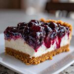 A close-up of a rich slice of blueberry cheesecake with a thick graham cracker crust and glossy blueberry topping.