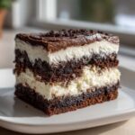 Close-up of a rich slice of brownie refrigerator cake showing alternating dark chocolate cake and white creamy layers.