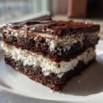 A rich slice of brownie refrigerator cake showing three dark chocolate layers separated by white cream filling.