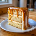 A decadent slice of layer cake with white frosting and thick, dripping caramel cake topping.