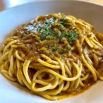 A close-up shot of rich, creamy caramelized onion pasta tossed with spaghetti and garnished with fresh parsley.