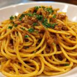 A close-up shot of perfectly twirled spaghetti coated in a rich sauce, featuring caramelized onion pasta, garnished with fresh parsley.