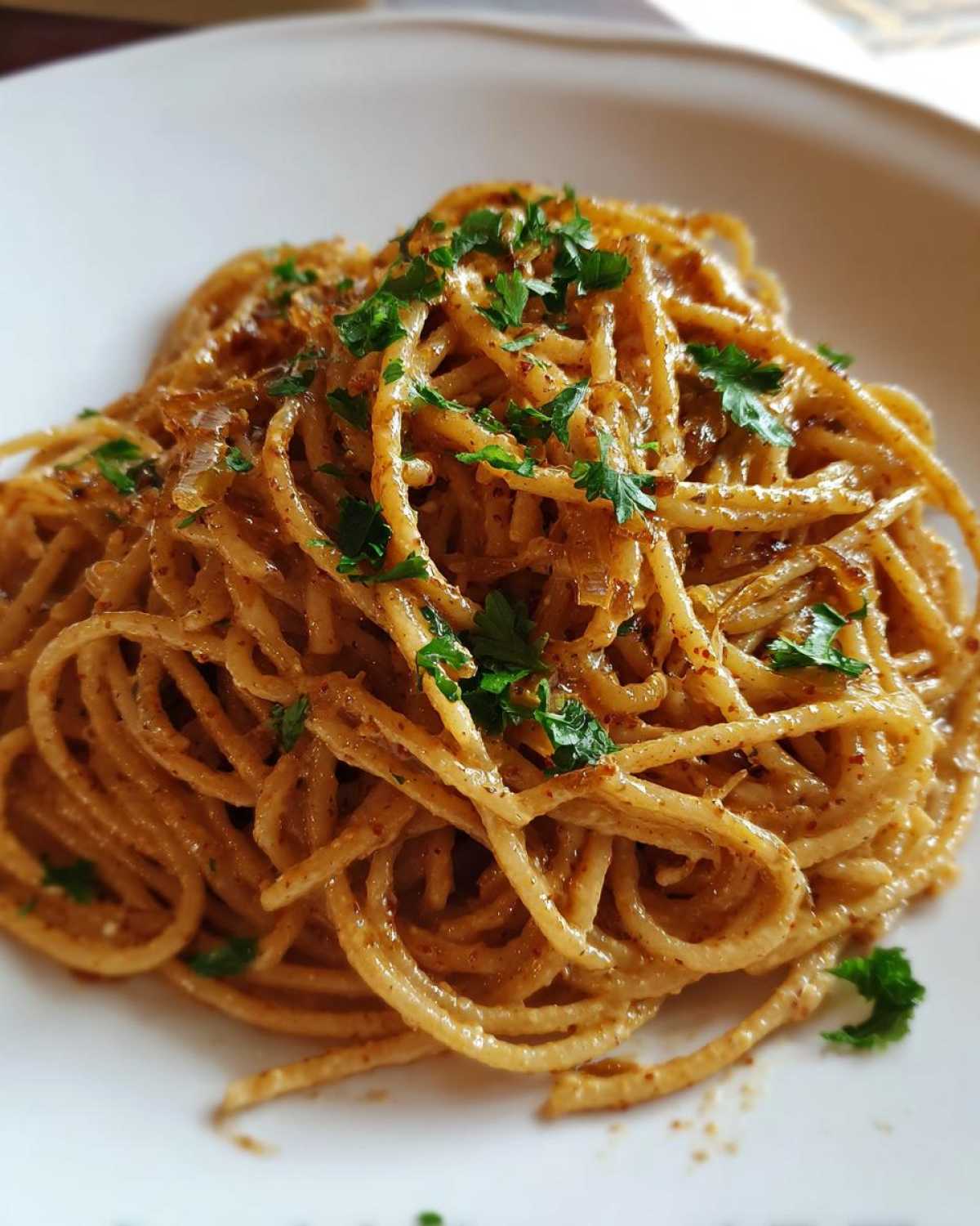 A close-up of a serving of amazing caramelized onion pasta tossed in a rich sauce and topped with fresh parsley.