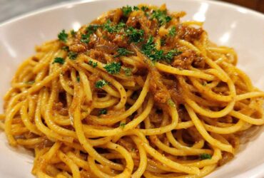 A close-up shot of perfectly twirled spaghetti coated in a rich sauce, featuring caramelized onion pasta, garnished with fresh parsley.