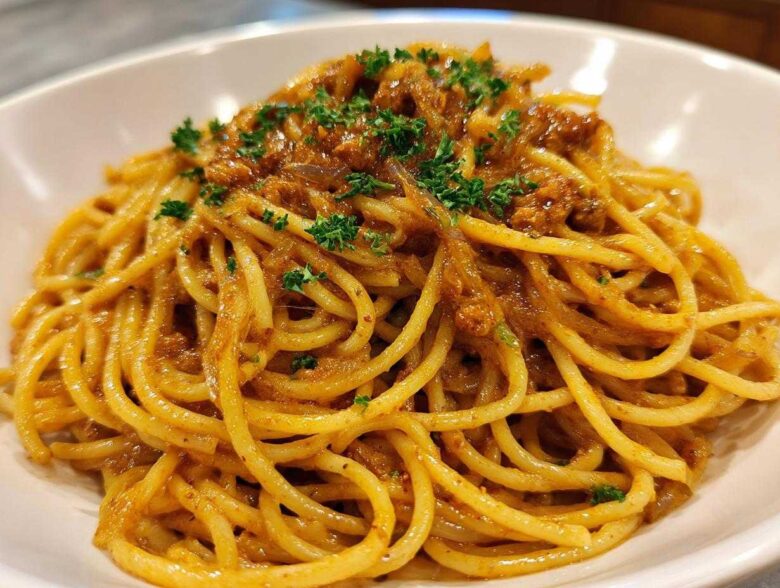 A close-up shot of perfectly twirled spaghetti coated in a rich sauce, featuring caramelized onion pasta, garnished with fresh parsley.