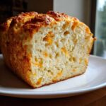 A close-up of a slice of homemade beer bread, showing a fluffy interior studded with melted cheddar cheese.