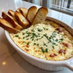 Close-up of a hot, cheesy bread dip topped with parsley, served with toasted bread slices for dipping.