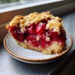 Close-up of a moist slice of cherry dump cake with a crumbly topping on a small plate.