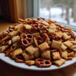 A large white platter piled high with homemade chex party mix, featuring cereal squares and pretzels.