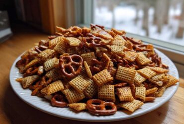 A large white platter piled high with homemade chex party mix, featuring cereal squares and pretzels.