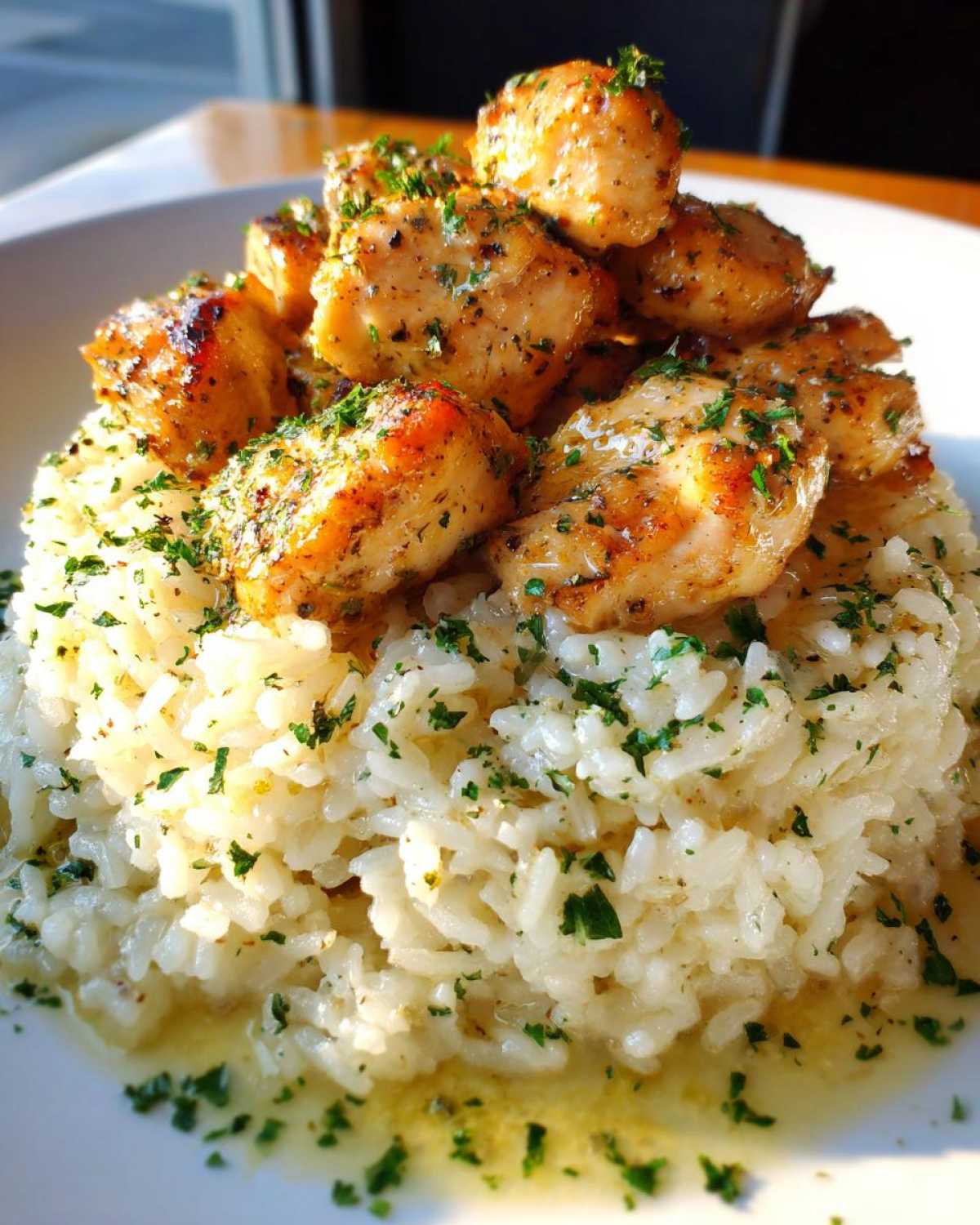 Golden pan-seared chicken pieces served over a mound of creamy garlic parmesan rice, garnished with parsley.