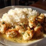 Close-up of tender chicken scampi pieces swimming in lemon-butter sauce next to a mound of white rice.