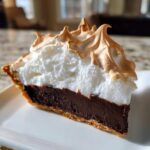 A perfect slice of chocolate meringue pie showing rich dark filling and tall, toasted meringue.