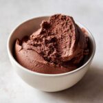 A close-up of a generous scoop of rich, dark chocolate mousse served in a small, light-colored ceramic bowl.