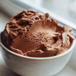 A close-up of rich, airy chocolate mousse scooped into a small, rustic white bowl.