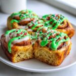 Close-up of fluffy christmas tree cinnamon rolls topped with white and bright green icing and festive red and green sprinkles.