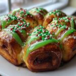 Close-up of freshly baked christmas tree cinnamon rolls arranged in a circle, topped with bright green icing and red, white, and green sprinkles.