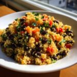 Close-up of a vibrant cilantro lime quinoa salad with black beans and diced orange/red peppers in a white bowl.
