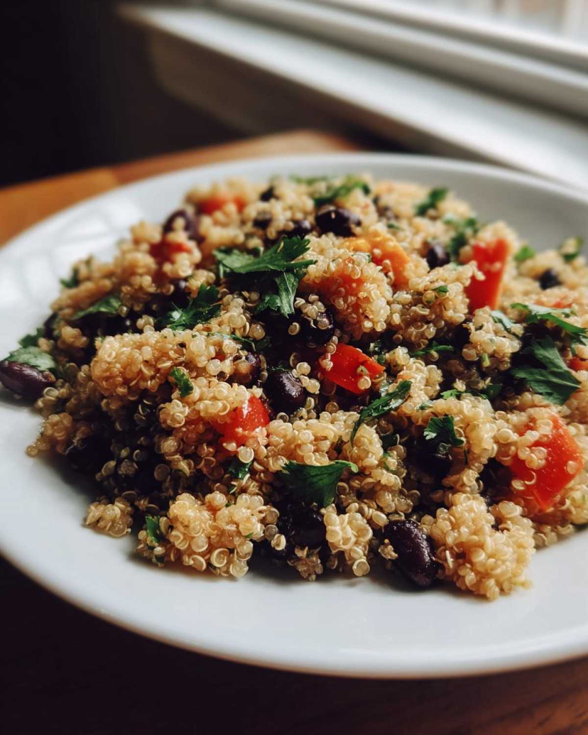 Close-up of a vibrant cilantro lime quinoa salad mixed with black beans and diced red peppers on a white plate.