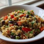 Close-up of a bright cilantro lime quinoa salad with black beans and diced red tomatoes in a white bowl.