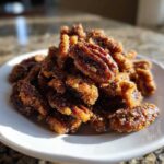 A close-up, sunlit pile of freshly made cinnamon sugar pecans coated in sparkling sugar crystals on a white plate.