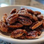 Close-up of glossy, candied cinnamon sugar pecans piled high in a small white bowl.