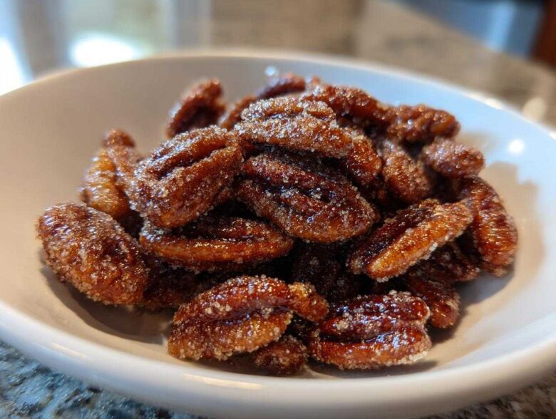 Close-up of glossy, candied cinnamon sugar pecans piled high in a small white bowl.
