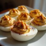 Close-up of six classic deviled eggs arranged on a white plate, topped with piped yolk filling and paprika.