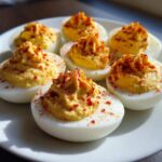 A plate of six beautifully made classic deviled eggs, topped with a swirl of creamy filling and sprinkled with paprika.