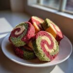 Close-up of colorful red, green, and cream pinwheel cookies stacked on a white plate.