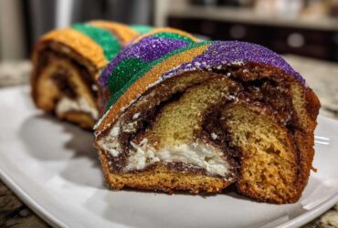Close-up of a slice of cream cheese king cake showing swirled dough, filling, and purple, green, and gold sanding sugar.