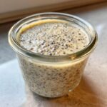 Close-up of creamy chia seed pudding, showing soaked chia seeds suspended in a light-colored liquid inside a glass jar.