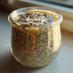 A close-up shot of creamy chia seed pudding prepared in a small glass jar, set against bright window light.