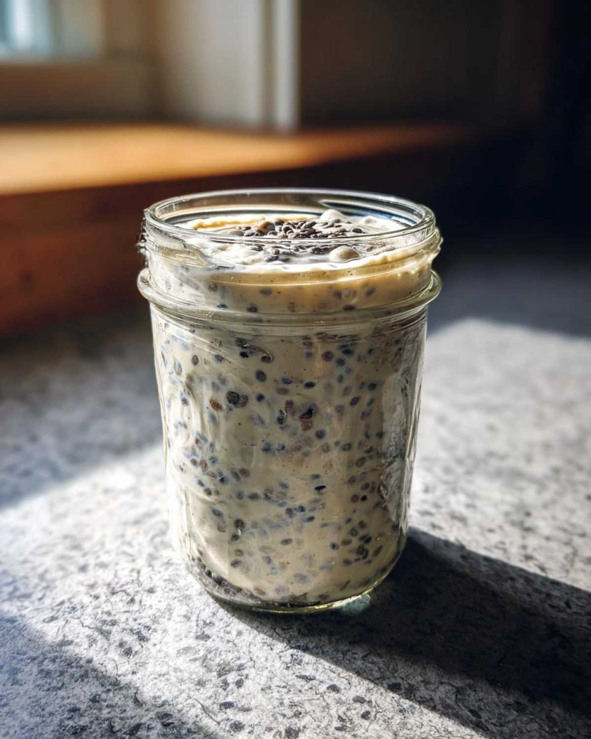 Close-up of creamy chia seed pudding prepared in a glass mason jar, topped with extra seeds.