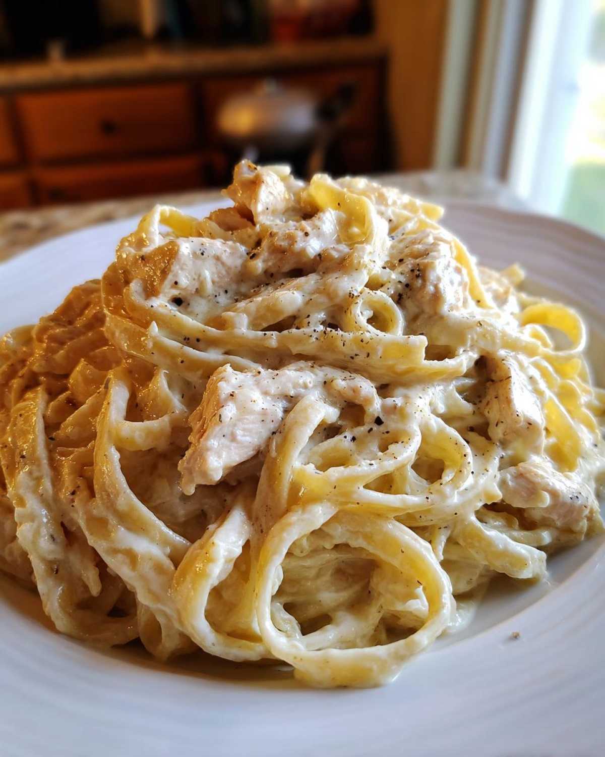 Close-up of a generous serving of creamy chicken fettuccine alfredo pasta, topped with cracked black pepper.