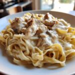 Close-up of a serving of creamy chicken fettuccine alfredo pasta topped with chunks of seasoned chicken.