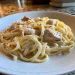 Close-up of creamy chicken fettuccine alfredo pasta generously coated in white sauce and sprinkled with pepper.