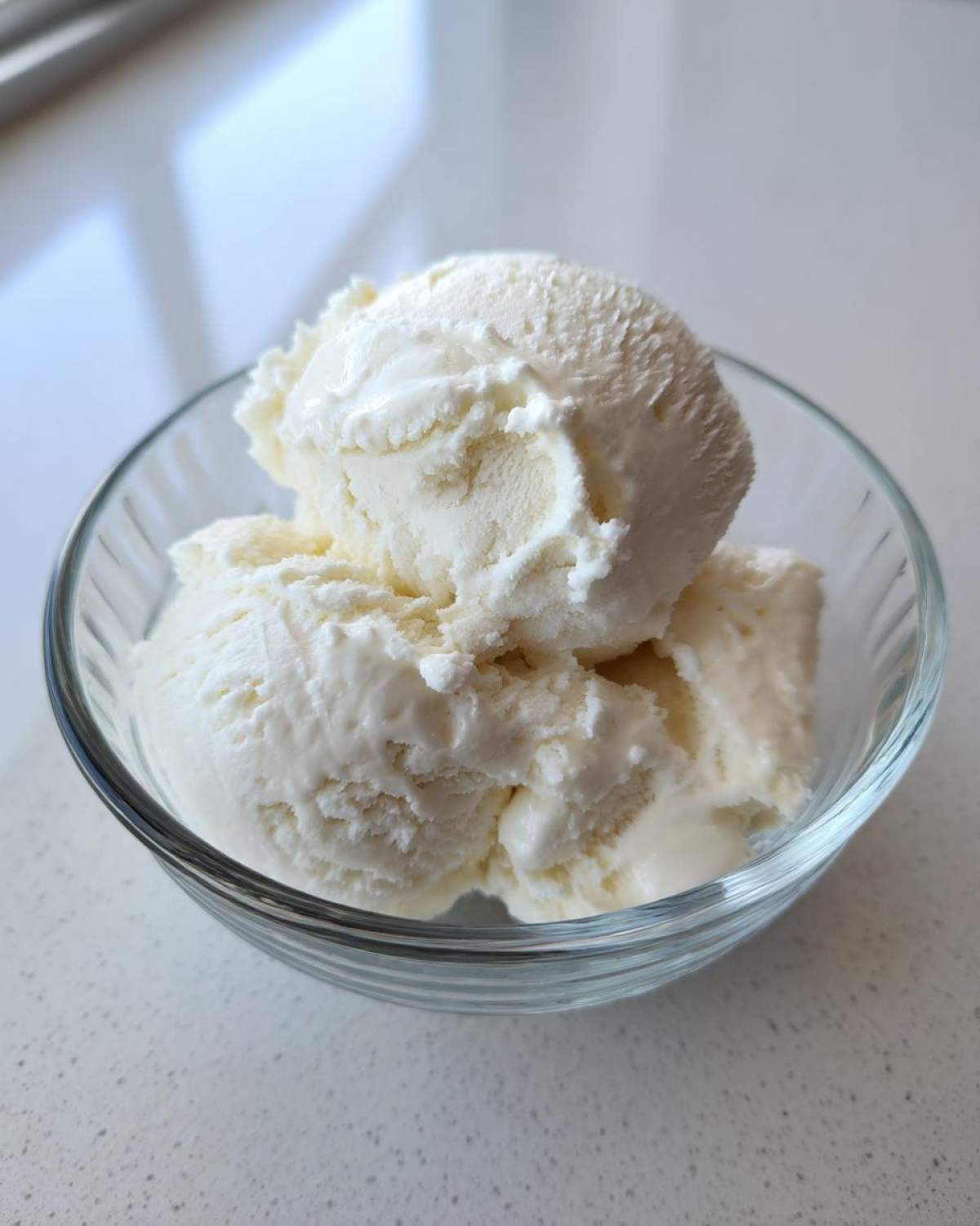 Two scoops of creamy, white cottage cheese ice cream served in a small glass bowl.