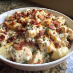 Close-up of a white bowl filled with creamy crack chicken gnocchi, topped with crispy bacon bits and parsley.